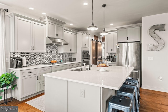 kitchen featuring a center island with sink, under cabinet range hood, a sink, a kitchen breakfast bar, and stainless steel appliances