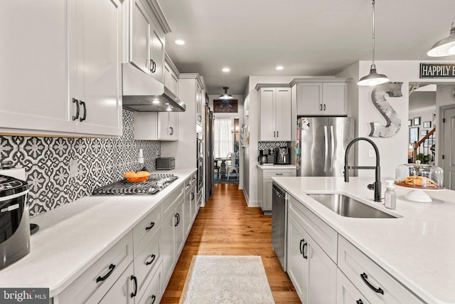 kitchen featuring under cabinet range hood, a sink, light wood-style floors, appliances with stainless steel finishes, and light countertops