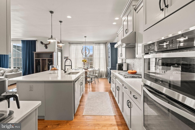 kitchen with light wood finished floors, a sink, stainless steel appliances, light countertops, and under cabinet range hood