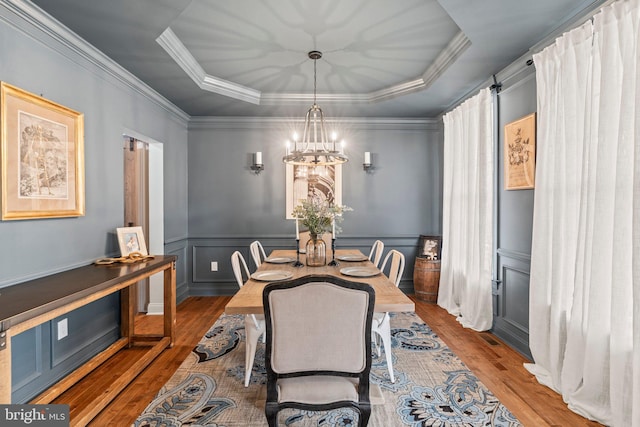 dining area with wood finished floors, a wainscoted wall, a tray ceiling, ornamental molding, and a notable chandelier