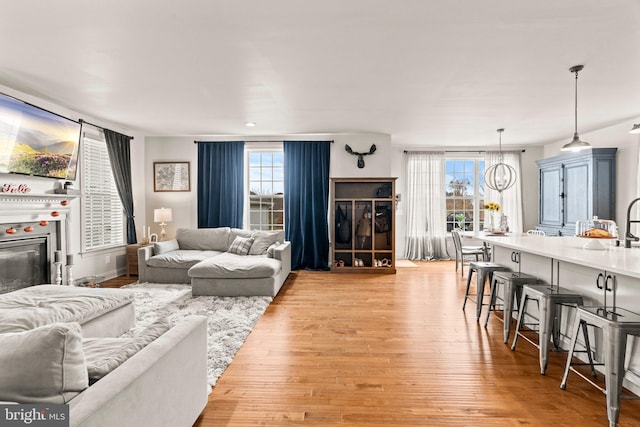 living area with a glass covered fireplace, an inviting chandelier, and light wood-type flooring