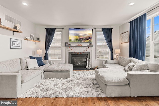 living area featuring a glass covered fireplace, recessed lighting, wood finished floors, and visible vents