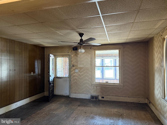 interior space with visible vents, a drop ceiling, wood walls, and hardwood / wood-style flooring