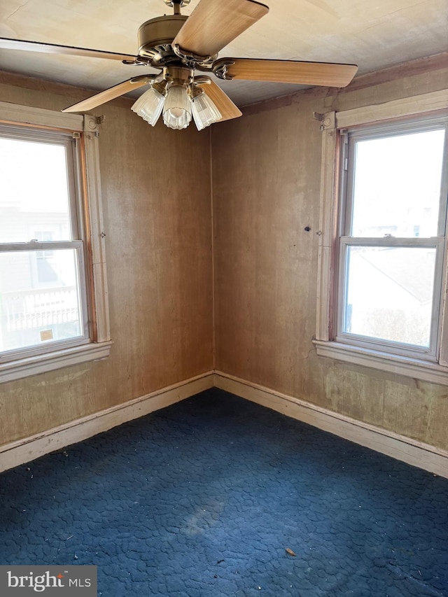 unfurnished room with wooden walls, baseboards, dark carpet, and ceiling fan