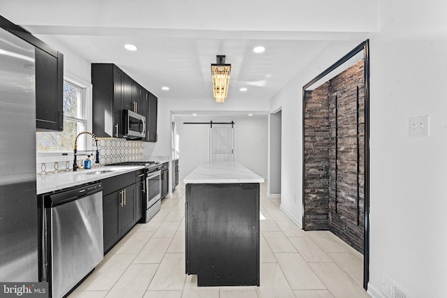 kitchen with a sink, dark cabinetry, a center island, a barn door, and appliances with stainless steel finishes