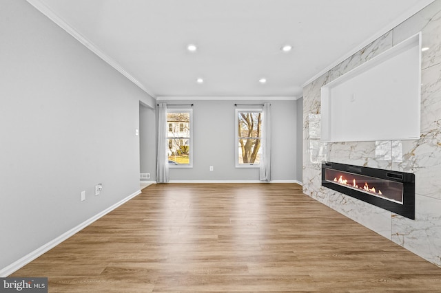 unfurnished living room with light wood-type flooring, a high end fireplace, recessed lighting, crown molding, and baseboards