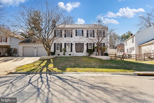 colonial-style house with an attached garage, concrete driveway, a front yard, and fence