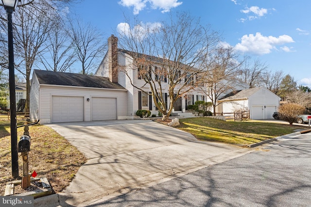 colonial home featuring a front yard, an attached garage, driveway, and a chimney