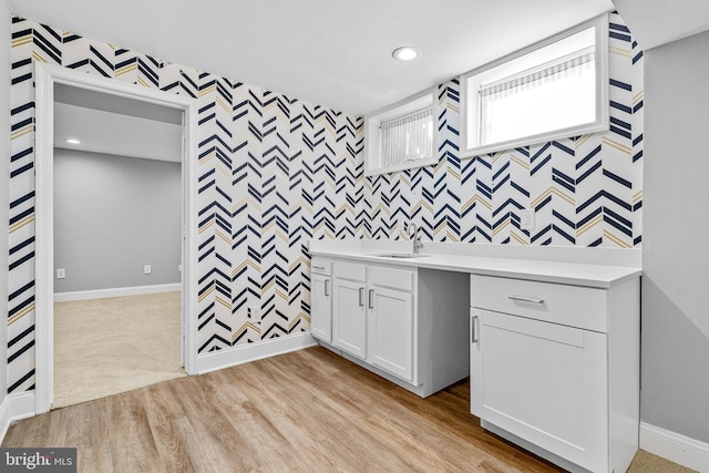 kitchen featuring wallpapered walls, an accent wall, baseboards, light countertops, and a sink