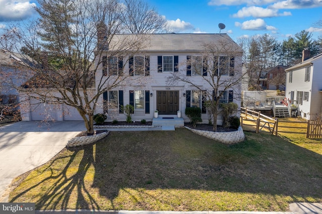 colonial-style house with driveway, fence, an attached garage, a front yard, and a chimney