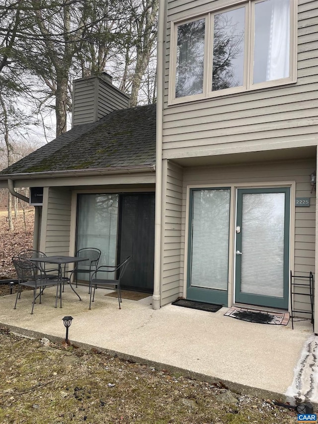 property entrance with a patio, roof with shingles, and a chimney