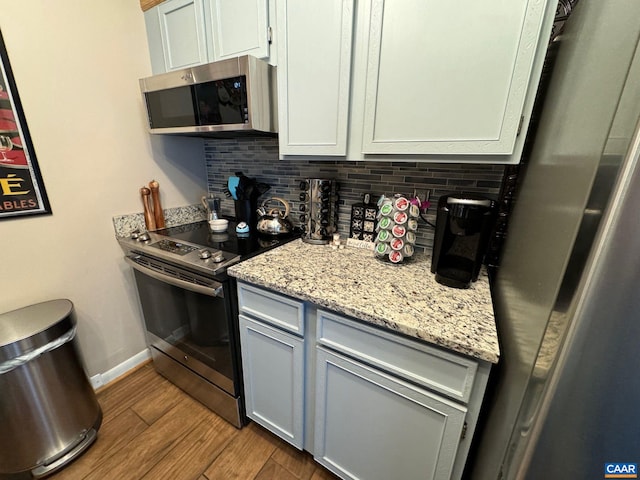 kitchen with light stone counters, tasteful backsplash, wood finished floors, appliances with stainless steel finishes, and baseboards