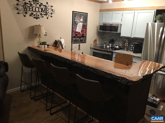 kitchen featuring backsplash, dark wood-type flooring, a breakfast bar area, appliances with stainless steel finishes, and white cabinets