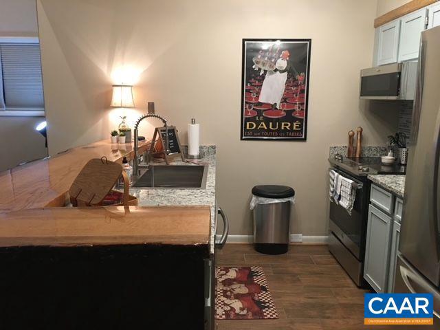 kitchen featuring light stone counters, baseboards, dark wood-style flooring, a sink, and appliances with stainless steel finishes