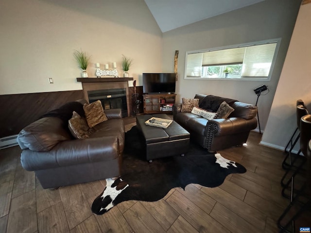 living area with wood finish floors, a baseboard heating unit, lofted ceiling, and a glass covered fireplace