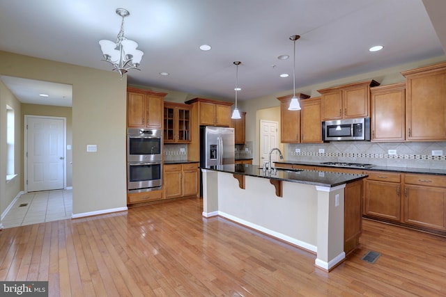 kitchen featuring a breakfast bar area, a center island with sink, light wood finished floors, appliances with stainless steel finishes, and brown cabinets