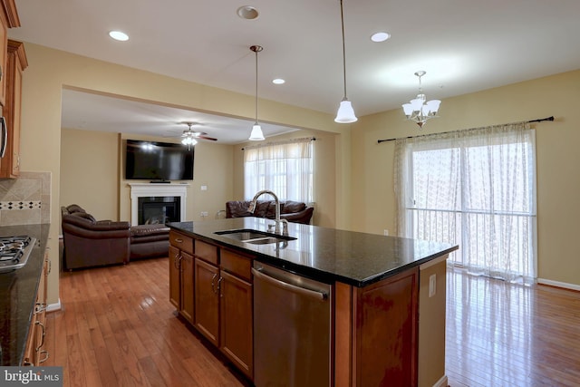 kitchen featuring brown cabinets, a sink, stainless steel appliances, a glass covered fireplace, and open floor plan