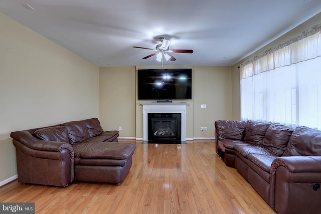 living room featuring a glass covered fireplace, ceiling fan, baseboards, and wood finished floors