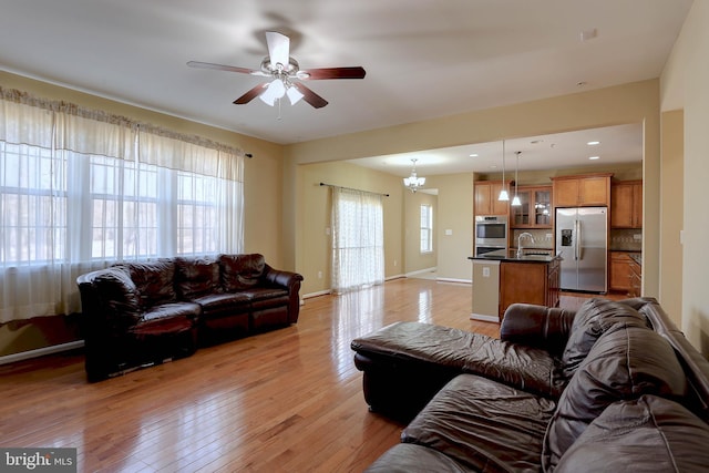 living room with light wood finished floors, ceiling fan with notable chandelier, and baseboards