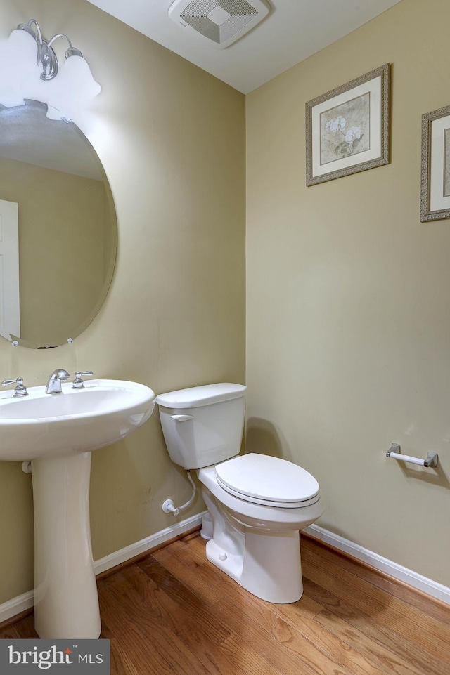 half bath with visible vents, toilet, baseboards, and wood finished floors