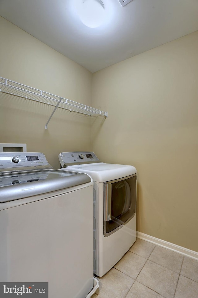 laundry room with laundry area, light tile patterned floors, washing machine and dryer, and baseboards