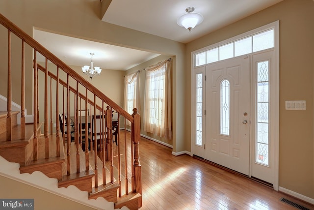 entryway with visible vents, hardwood / wood-style floors, stairway, an inviting chandelier, and baseboards