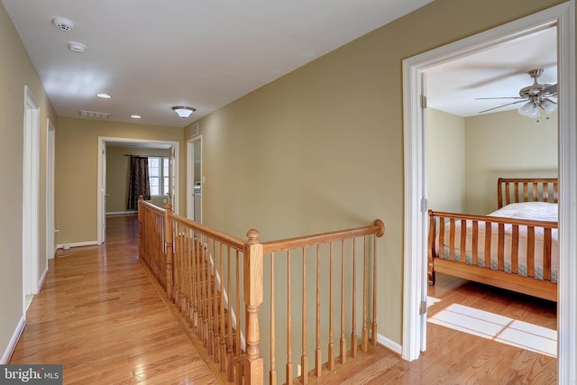 hallway featuring visible vents, an upstairs landing, baseboards, and light wood finished floors