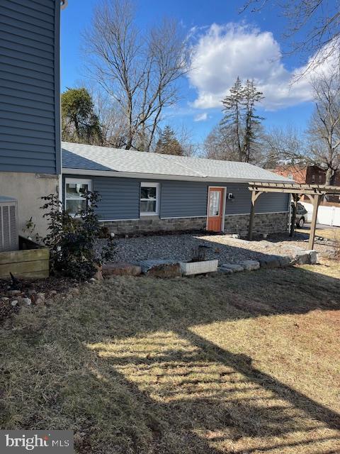 rear view of property featuring central air condition unit and a lawn