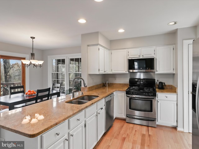 kitchen with light stone counters, a peninsula, a sink, appliances with stainless steel finishes, and white cabinetry