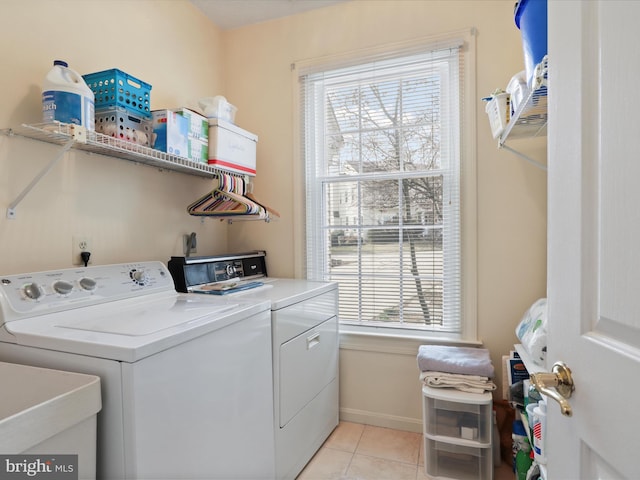 clothes washing area with light tile patterned floors, baseboards, washing machine and clothes dryer, laundry area, and a sink