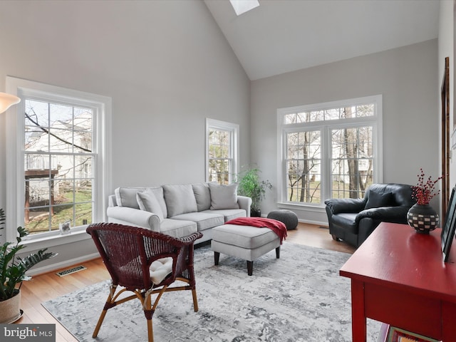 living area featuring baseboards, wood finished floors, high vaulted ceiling, and a skylight