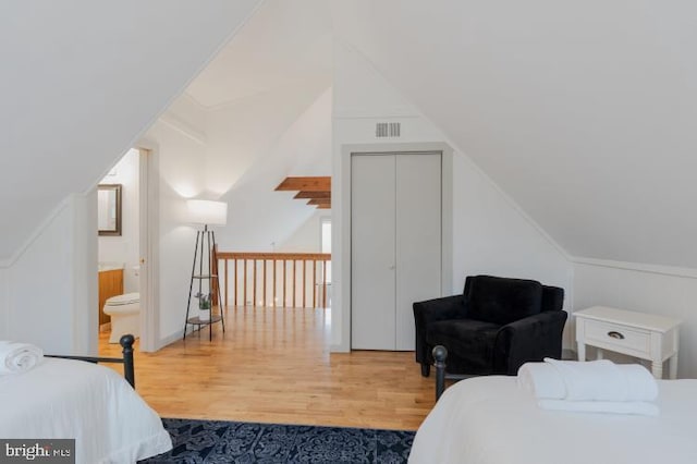 bedroom with visible vents, lofted ceiling, wood finished floors, and ensuite bathroom