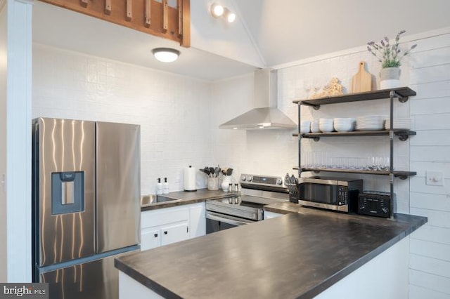 kitchen featuring dark countertops, appliances with stainless steel finishes, white cabinets, wall chimney range hood, and decorative backsplash