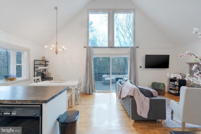 living room featuring light wood-type flooring, high vaulted ceiling, and a chandelier