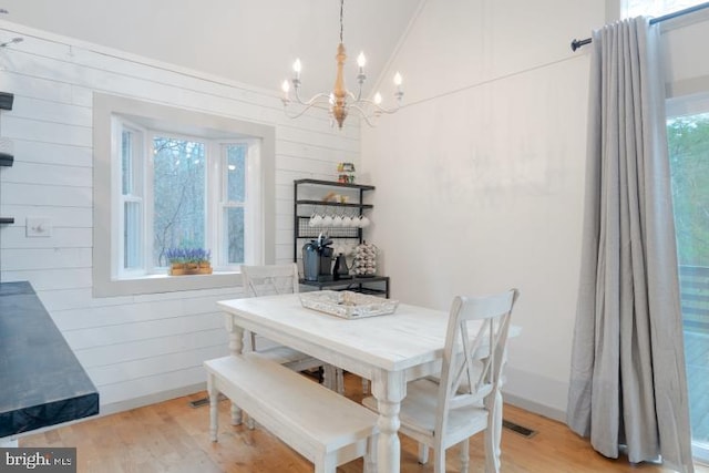 dining area with visible vents, light wood-style flooring, wooden walls, and vaulted ceiling