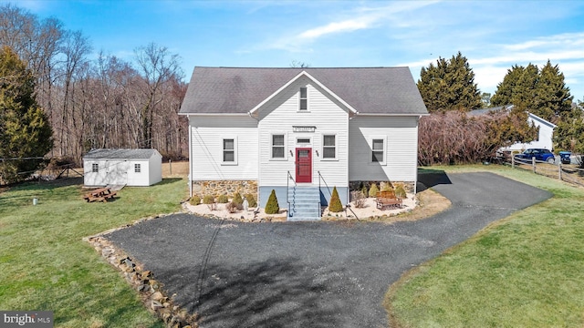 bungalow-style home with a storage unit, fence, roof with shingles, an outdoor structure, and a front yard