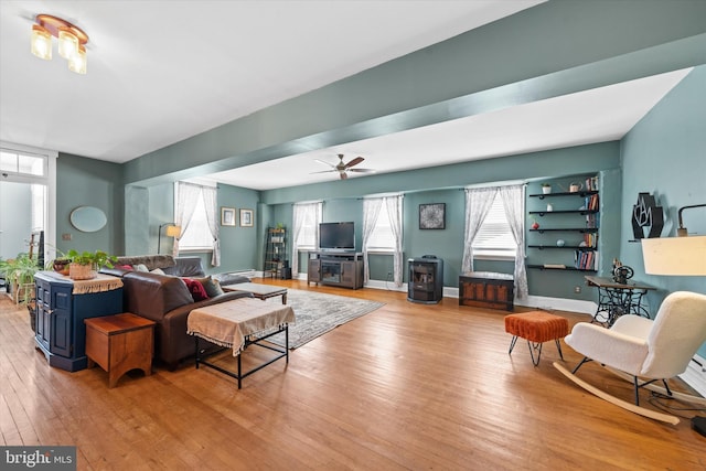 living area with hardwood / wood-style flooring, a wood stove, baseboards, and ceiling fan