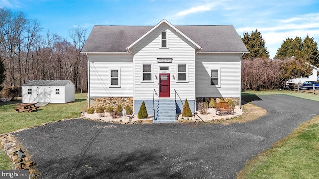 view of front of home with a front yard, a storage unit, an outbuilding, and a shingled roof