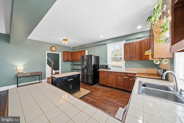 kitchen with a kitchen island, dark wood-style flooring, a sink, stainless steel appliances, and tile counters