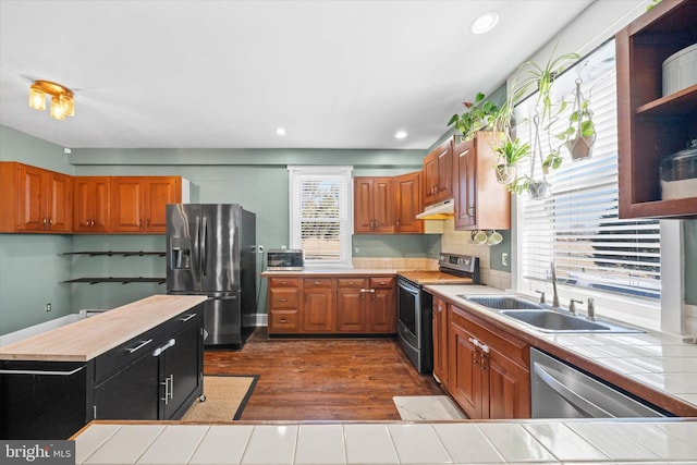 kitchen with under cabinet range hood, a sink, tile countertops, appliances with stainless steel finishes, and brown cabinetry