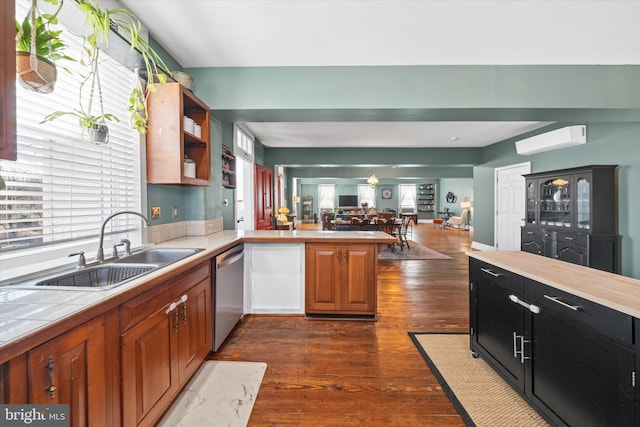 kitchen featuring a wall unit AC, tile countertops, a peninsula, a sink, and dishwasher