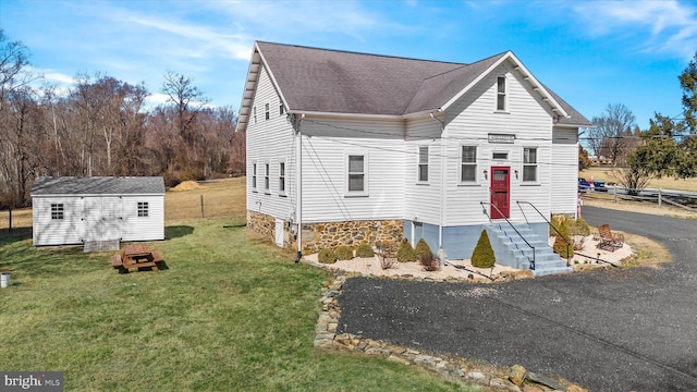 view of front of property featuring an outbuilding, driveway, fence, a front yard, and a shingled roof