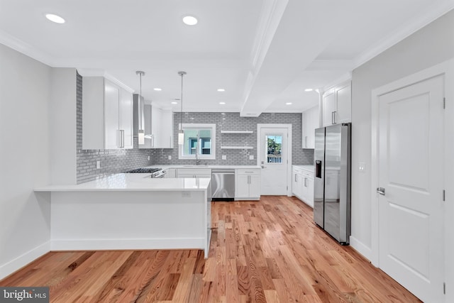 kitchen featuring a peninsula, ornamental molding, light countertops, light wood-style floors, and appliances with stainless steel finishes