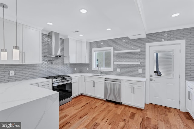 kitchen featuring a sink, white cabinets, appliances with stainless steel finishes, wall chimney range hood, and light wood-type flooring