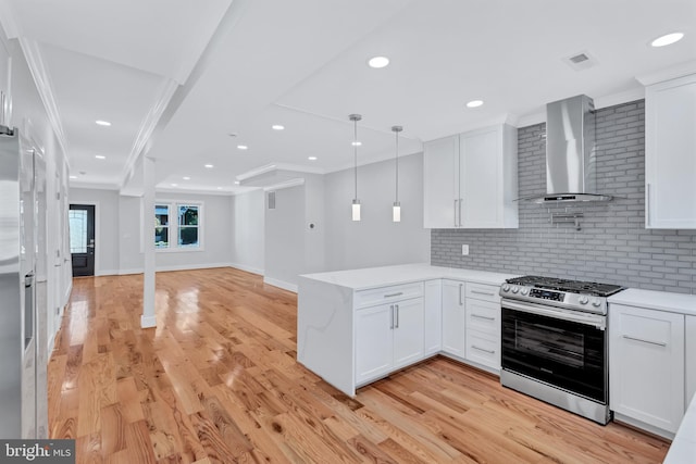 kitchen featuring a peninsula, white cabinets, wall chimney exhaust hood, light countertops, and stainless steel gas range