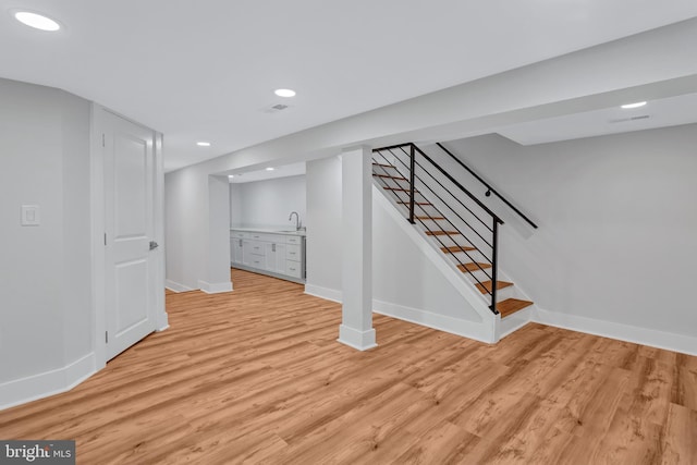 finished below grade area featuring stairway, baseboards, light wood finished floors, recessed lighting, and a sink