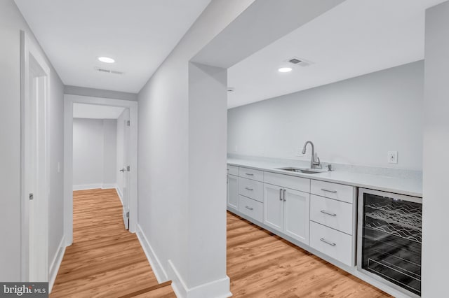 bar featuring a sink, visible vents, beverage cooler, and light wood finished floors