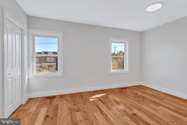 spare room with light wood-type flooring, visible vents, and baseboards