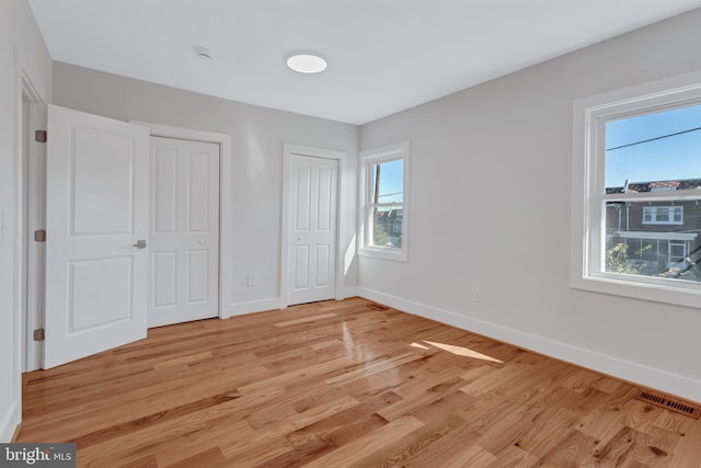 unfurnished bedroom with light wood-style floors, multiple windows, two closets, and baseboards