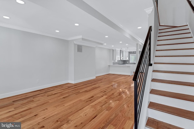 unfurnished living room with stairway, light wood-style floors, and crown molding